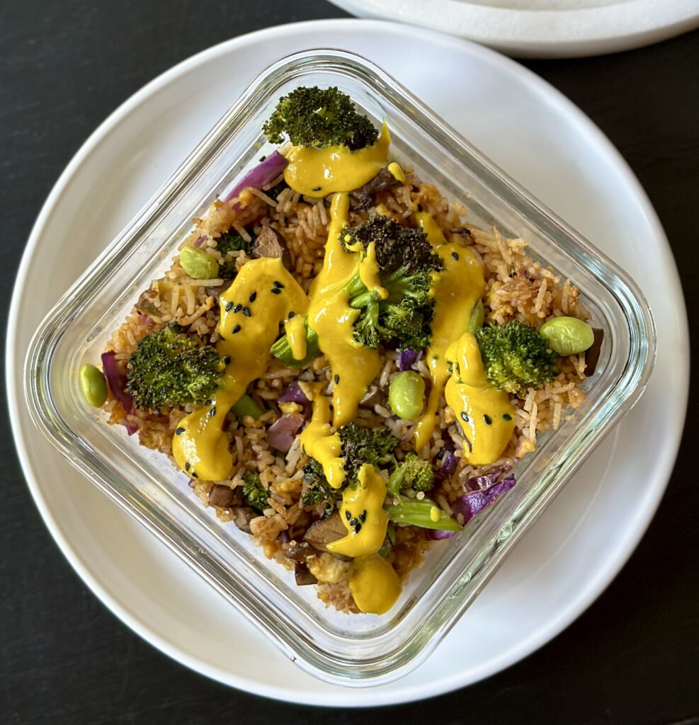 1 meal prep container with veggie fried rice with vibrant yellow miso turmeric dressing drizzled over top