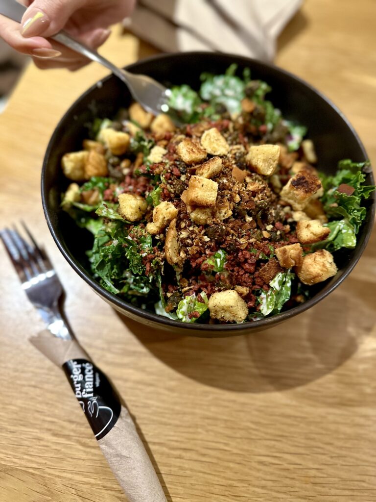 vegan kale salad from Burger Fiance. bowl of dressed lettuce, vegan bacon bits, and croutons.