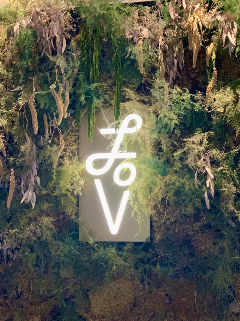 Photo of Lov's sign on a greenery wall