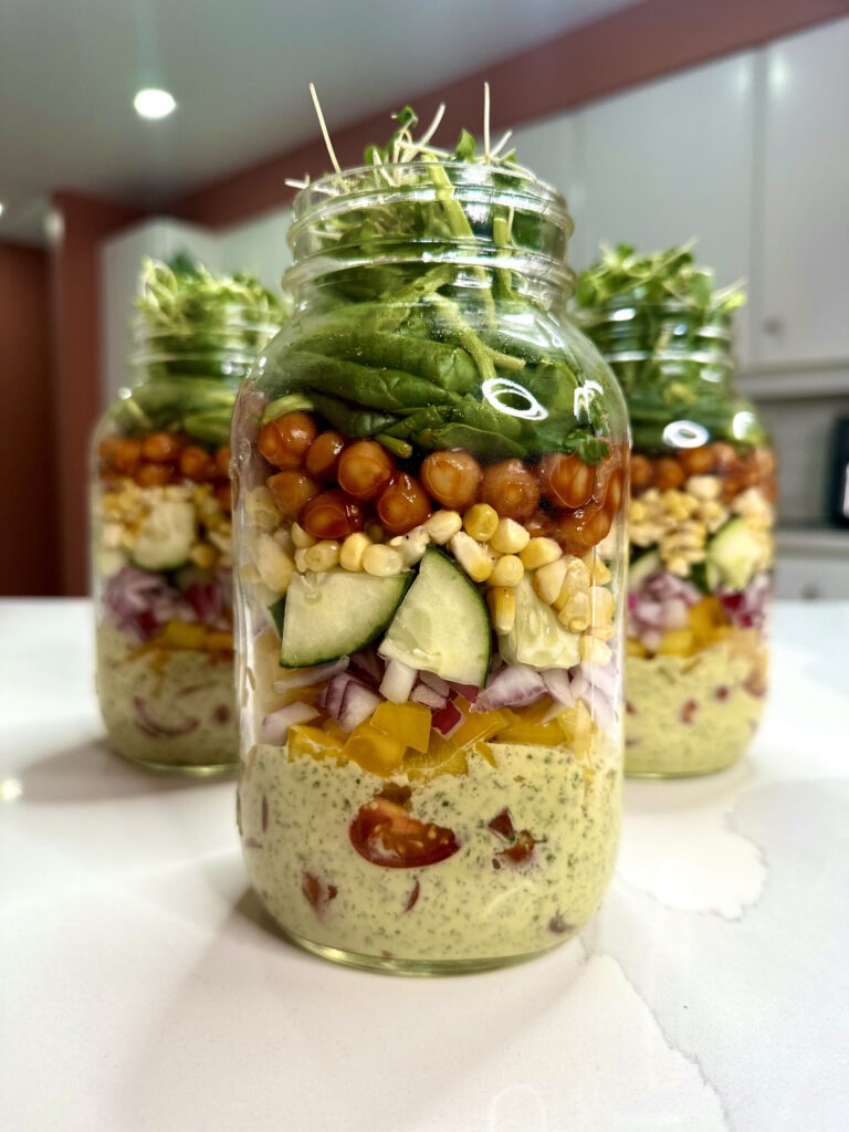 layered salad jar with herby ranch dressing, veggies, bbq chickpeas and lettuce on top