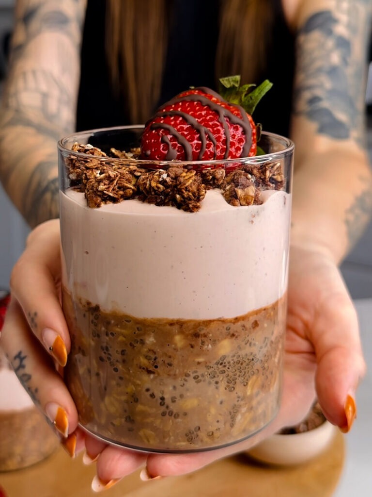 chocolate overnight oats with strawberry yogurt layer and chocolate granola and a strawberry on top. 