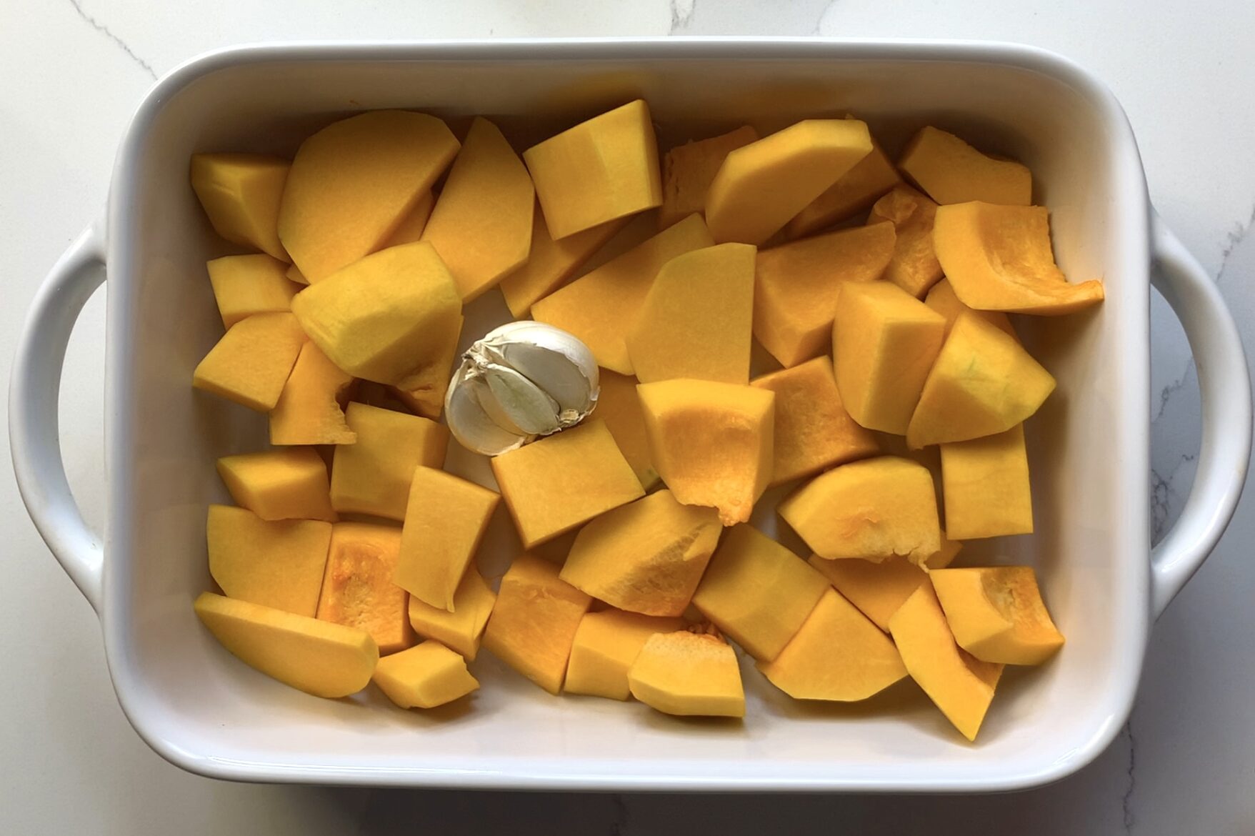 a tray of cubed butternut squash and garlic to be roasted