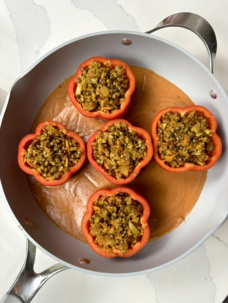 sauce pan with tomato béchamel sauce and loaded stuffed peppers on top