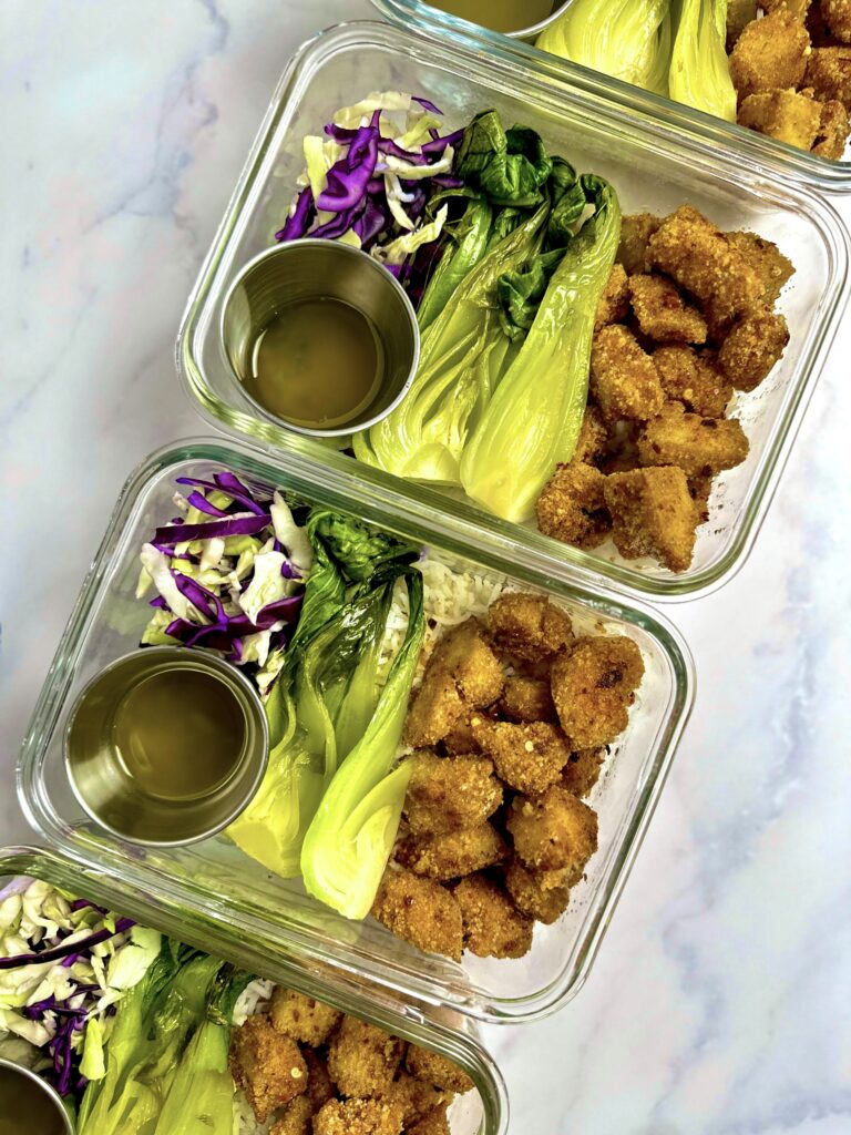 meal prep containers with rice, crispy tofu, hot and honey sauce,  bok choy, and coleslaw.