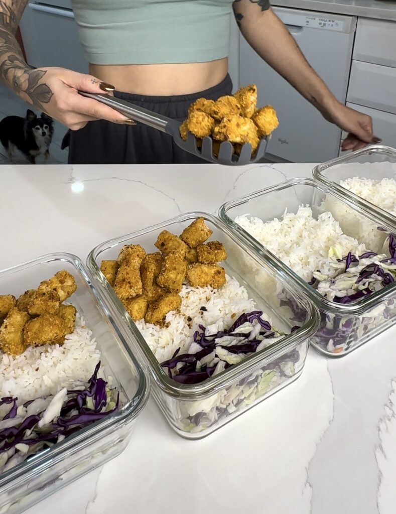 crispy tofu being added to meal prep containers with rice and coleslaw