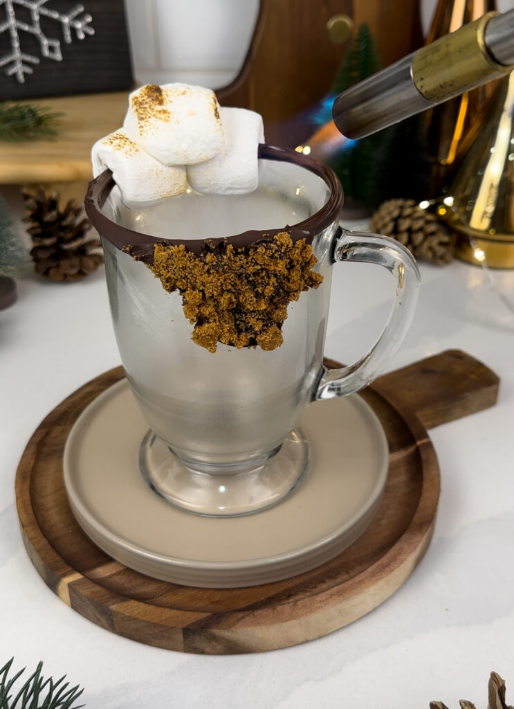 Mug with chocolate rim and marshmallows being toasted with a culinary torch.