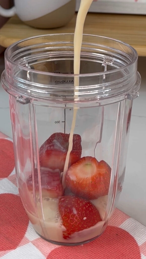 Making strawberry milk. Adding strawberry and non-dairy milk to blender container.