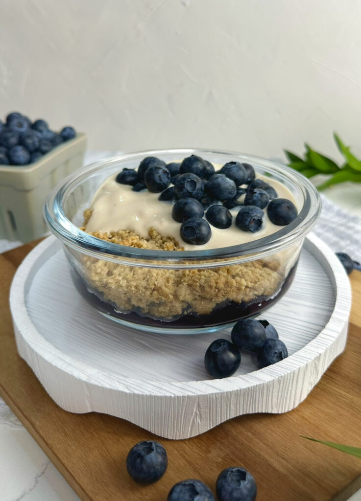 single meal prep container with blueberry layer on the bottom, shortcake crumble, topped with vanilla yogurt and fresh blueberries.