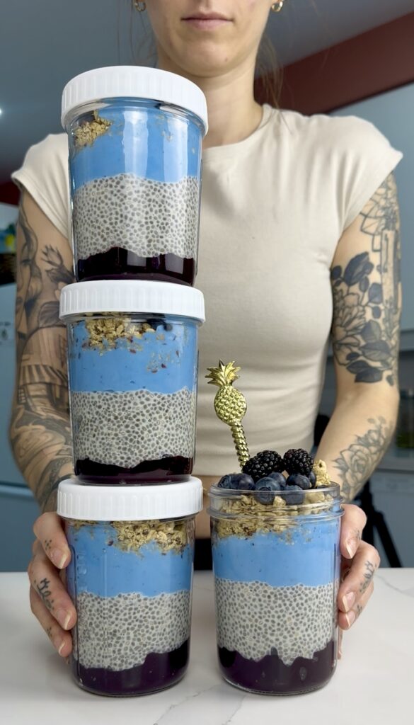 four meal prep jars layered with blueberry jam, vanilla chia seed pudding, blueberry yogurt and topped with granola and berries