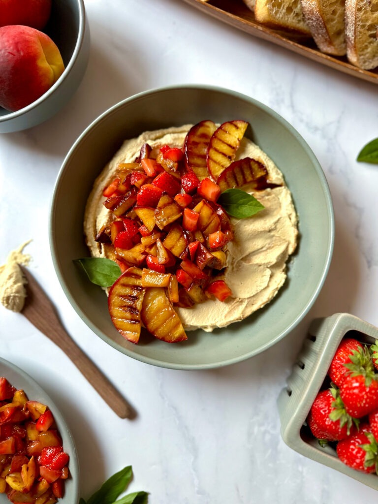 Bowl with whipped vegan tofu ricotta, grilled strawberries and peaches, topped with a balsamic glaze and fresh basil leaves. 
