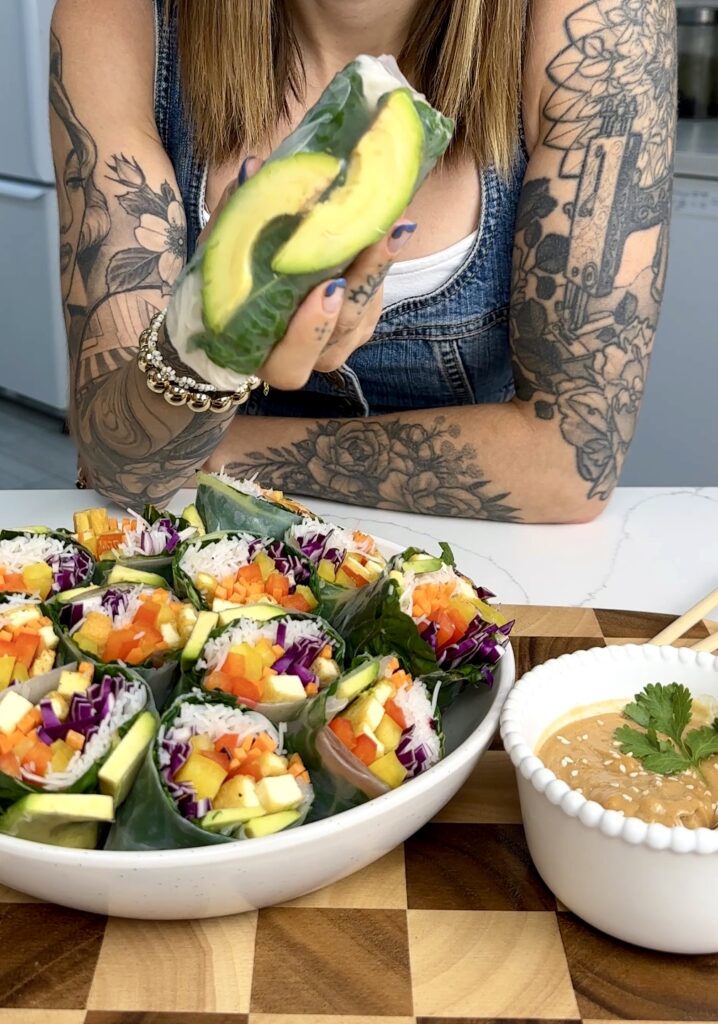 girl holding fresh summer roll with plate of summer rolls underneath 
