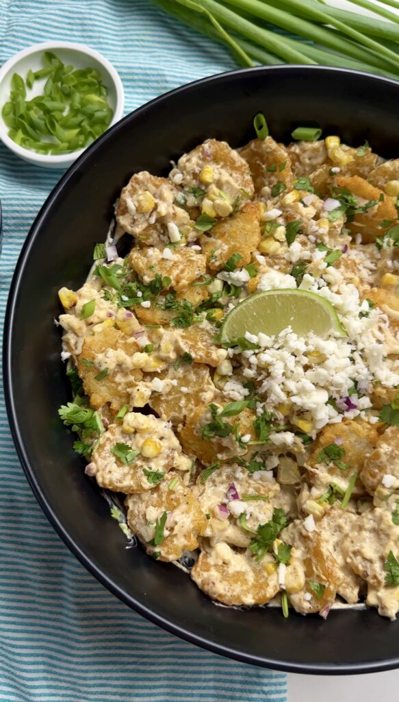 large bowl of tater tot sweet corn salad with a small bowl of green onion, on the side. 