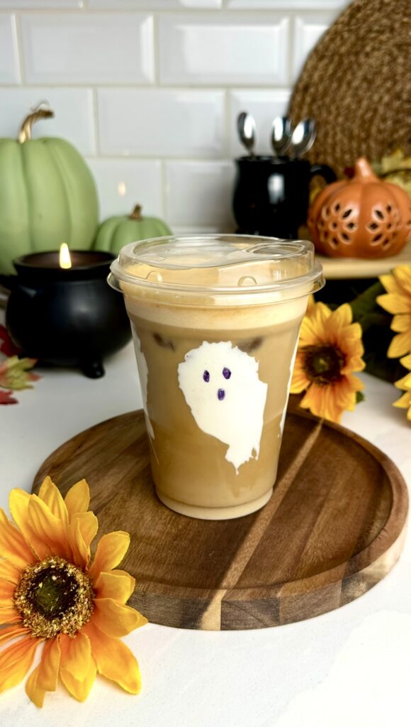 A plastic cup with ghosts made from marshmallow cream filled with an iced, toasted marshmallow latte and a silky pumpkin cold foam layer.