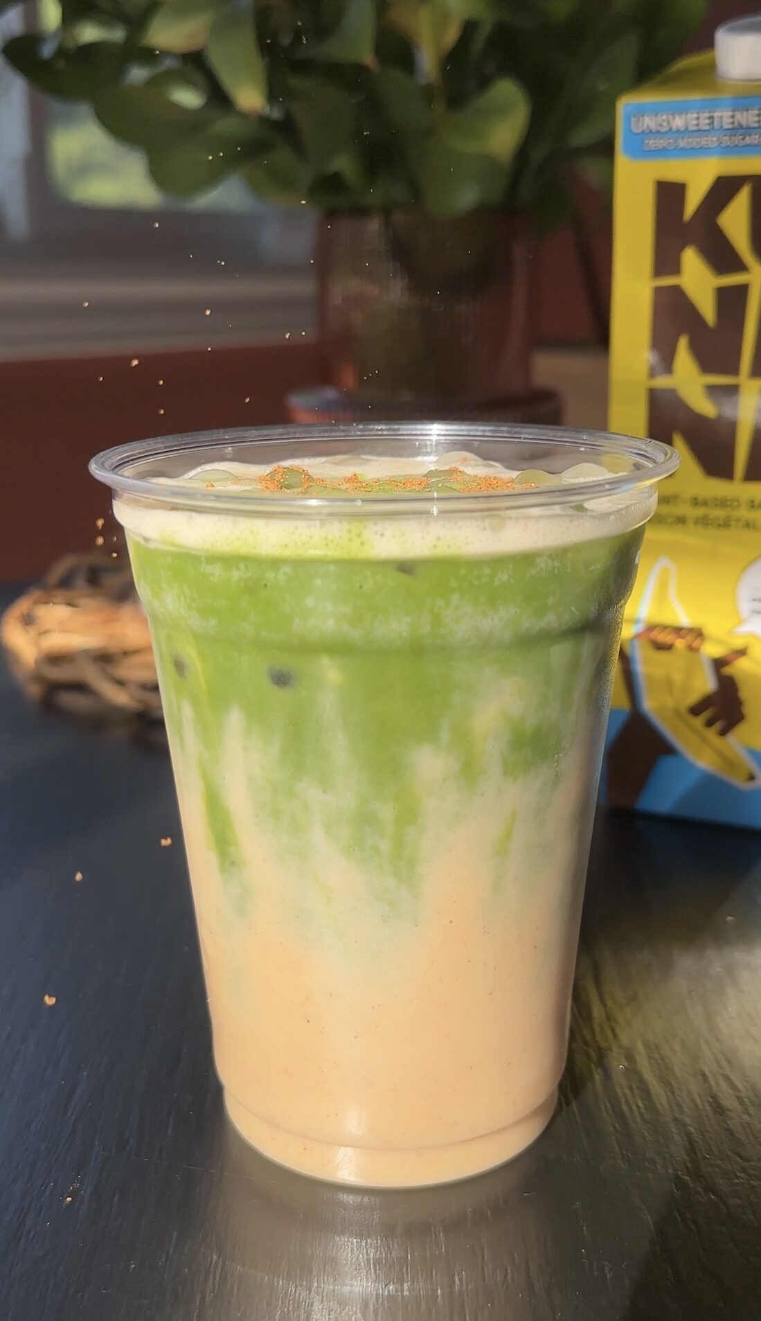 cinnamon being sprinkled on iced banana bread matcha latte
