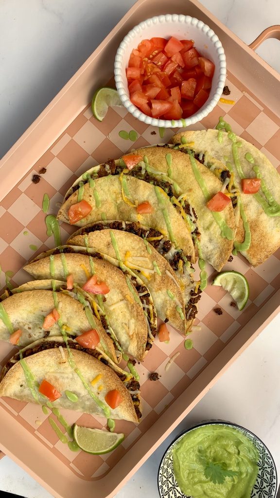 Finished tray of tacos with fresh toppings: cilantro, and diced red tomatoes with a cilantro lime drizzle.