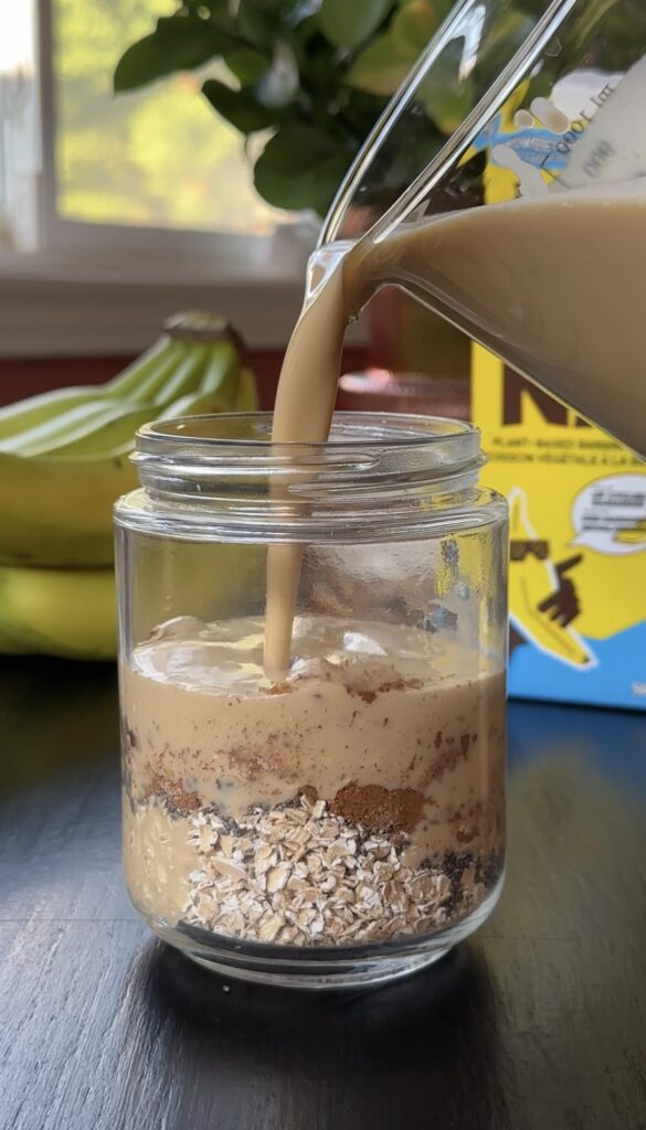 pouring banana milk over dry overnight oats ingredients.